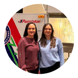 Two women stand side by side in front of a Purolator delivery e-bike, one wearing a burgundy long‑sleeve blouse and the other a light blue sweater. The graphic reads “International Women’s Day” and includes the quote: “As a young engineer woman in logistics, I had mentors that supported me and encouraged me to keep going.” Purolator branding appears below the quote.