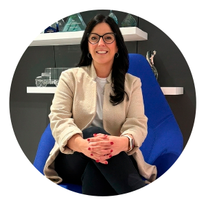 A woman wearing a beige jacket, black pants and glasses sits in a modern blue chair inside an office setting with her legs crossed and hands folded on her knee. “International Women’s Day” appears at the top of the graphic, along with the quote: “Giving my time through mentorship has provided a deep sense of purpose and connection.” Purolator branding is shown at the bottom below the quote.