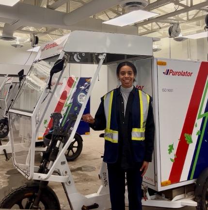 Oksana Dolson standing next to a Purolator electric vehicle delivery bike.