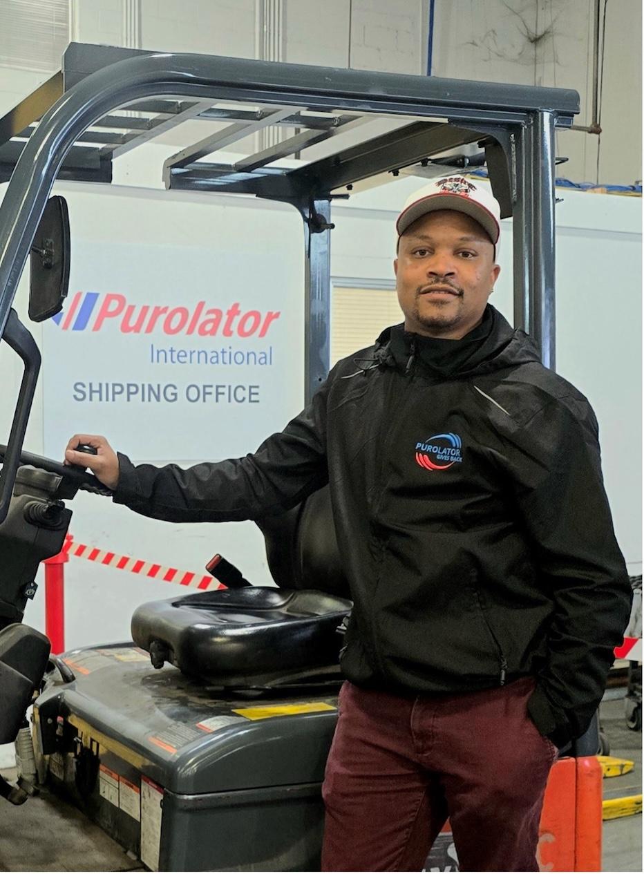 Leroy Oliver posing next to a heavy machinery in front of wall that says "Purolator International Shipping Office".
